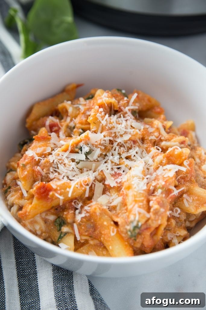 Close up of white bowl with baked ziti topped with cheese sitting on a blue and white striped kitchen towel. 