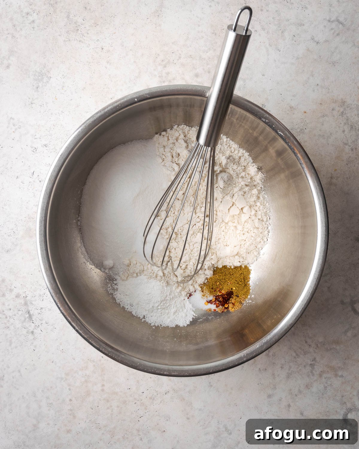 Gluten free flour, sugar, baking powder, salt and spices being whisked together in a metal mixing bowl.