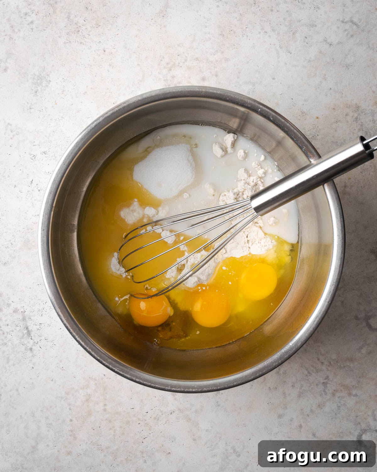 Eggs and milk added to the dry ingredients in a metal mixing bowl.