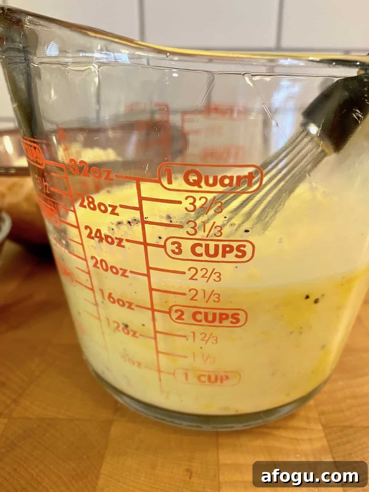 Eggs and milk whisked together in a glass measuring cup.