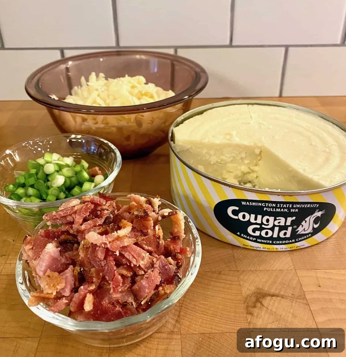 Small bowls of cooked, diced bacon, green onions and shredded cheese with an opened can of Cougar Gold on the side.