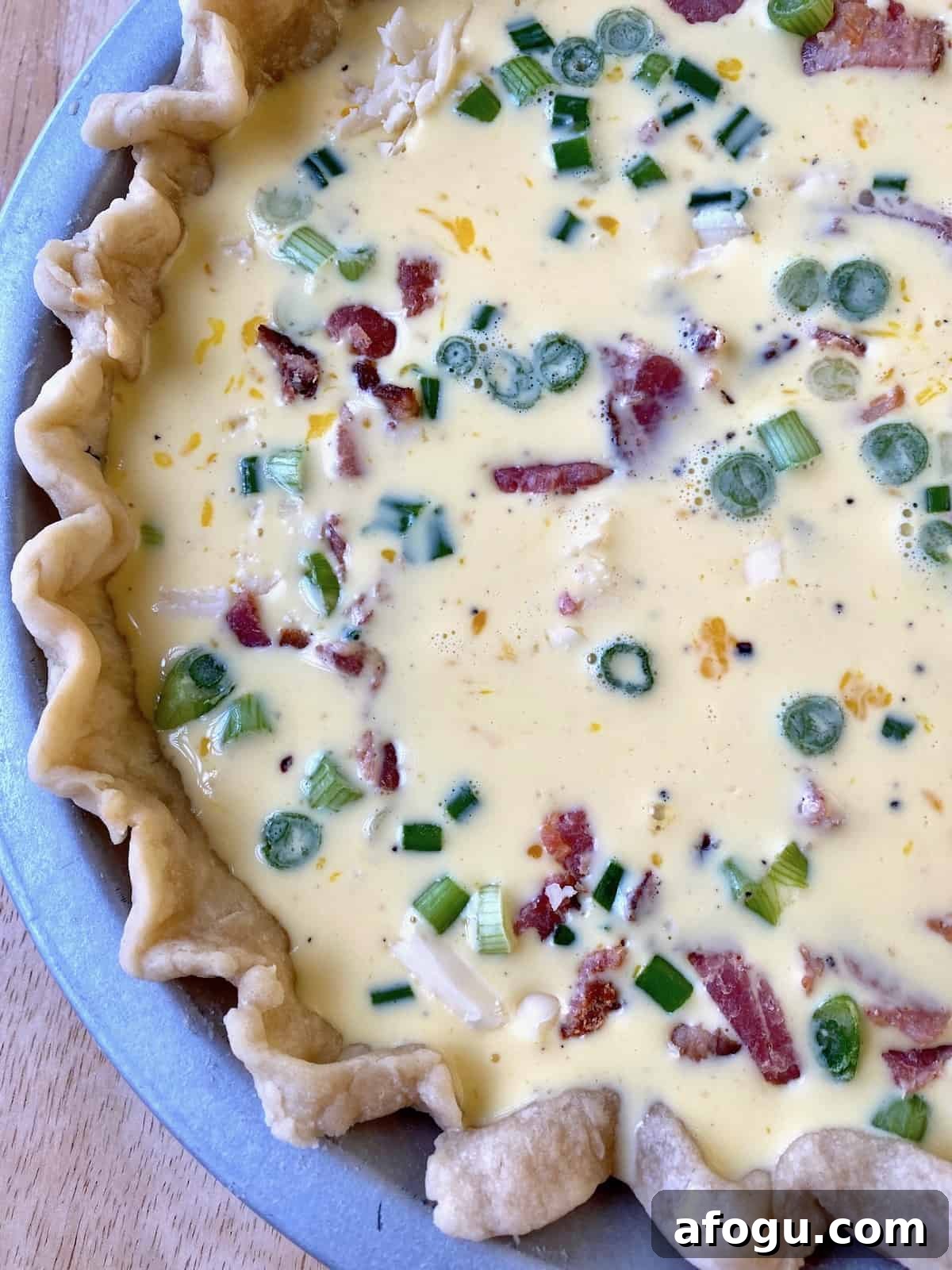 Unbaked quiche with bacon and diced green onions.