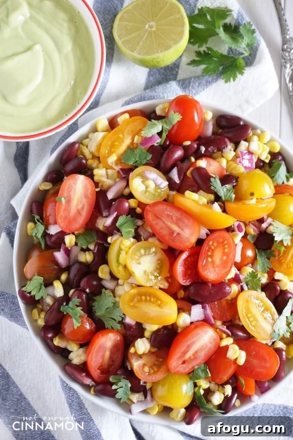 close-up of a bowl of corn, black bean & tomato salad with vegan avocado lime dressing on the side